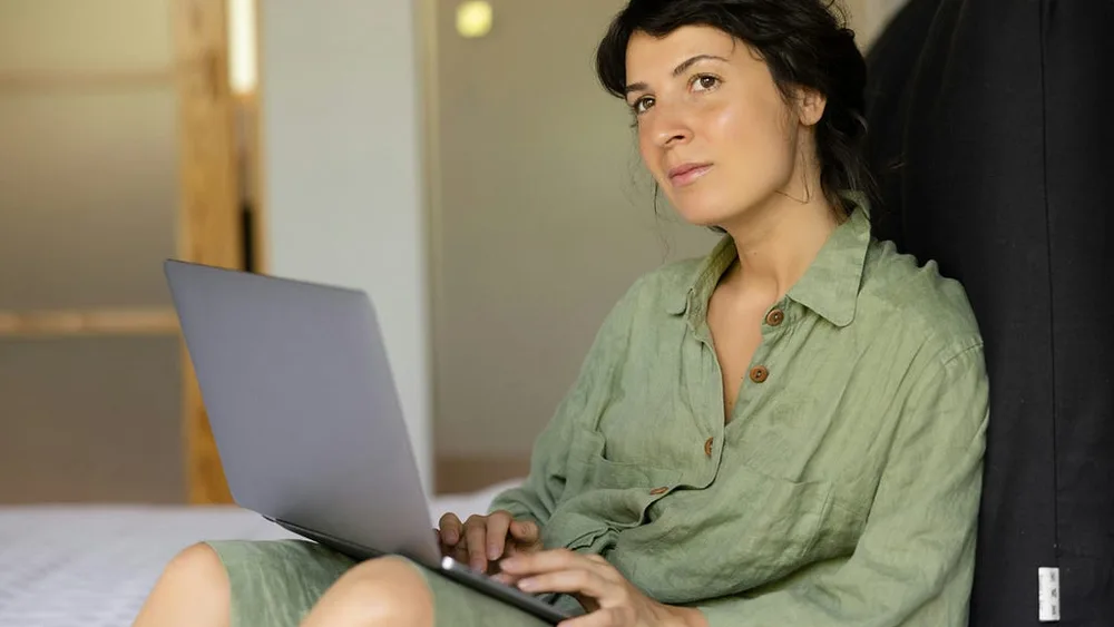 Woman pausing beside a laptop while reflecting on her availability and boundaries