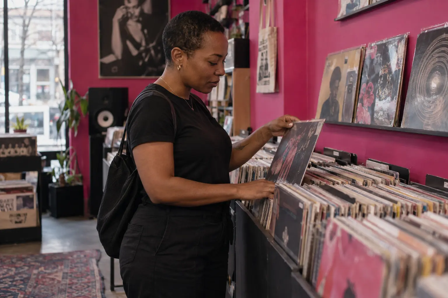 Woman browsing vinyl records in a shop with a magenta wall.