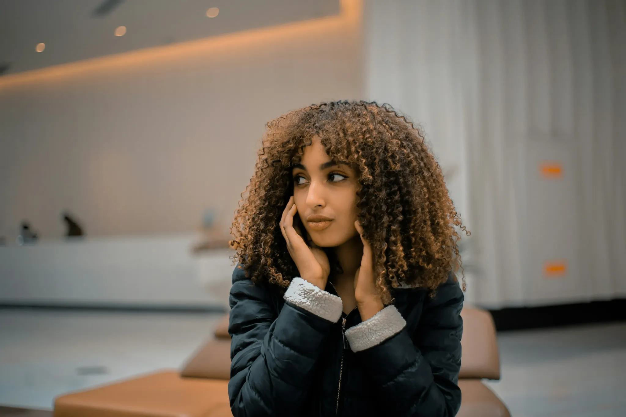 A woman seated in a quiet neutral space, looking reflective