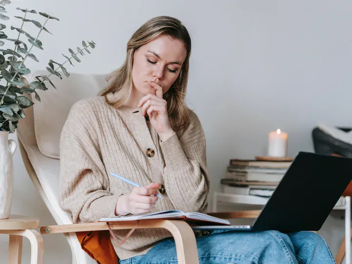 Woman thoughtfully planning in a notebook beside her laptop